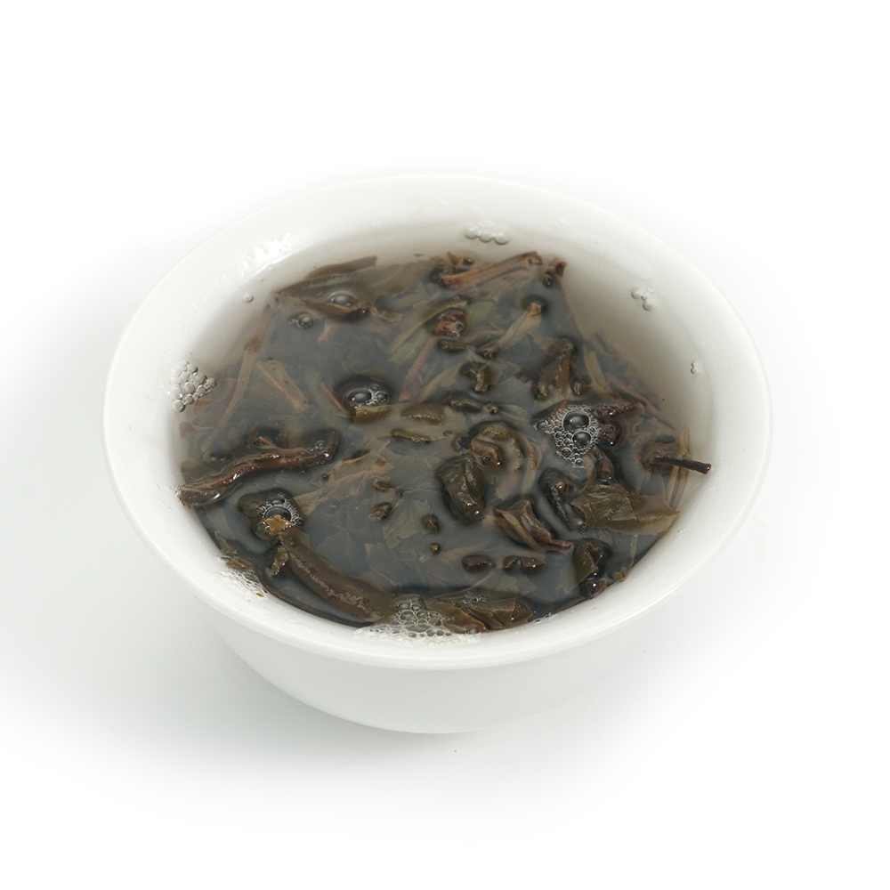 Aged Raw Pu’er tea infusion (2012 Fengpai) in a glass cup showing rich, oily amber tones.