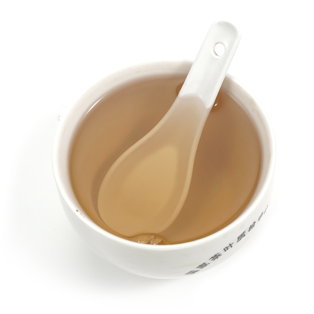 Deep golden-amber tea liquor of 2015 Aged White Tea in a porcelain cup, capturing its sweet plum essence.